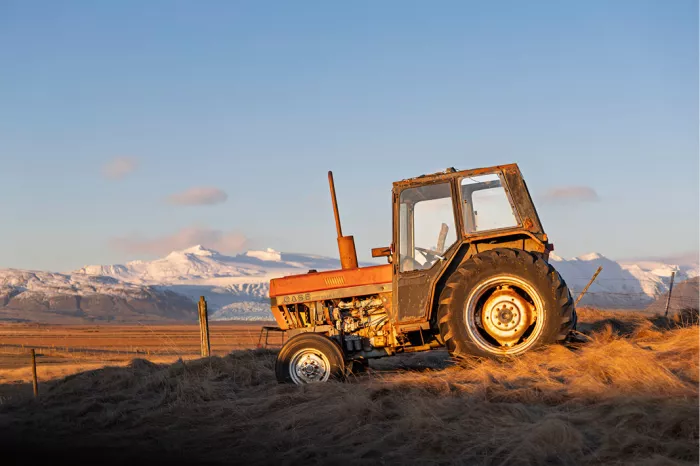 Oude oranje tractor op een heuvel met droog gras in avondlicht, met besneeuwde bergen op de achtergrond