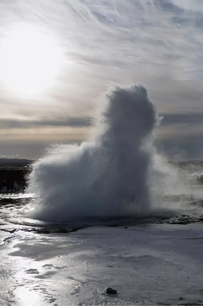 Uitbarstende geiser met een witte waterkolom in tegenlicht boven een natte vlakte