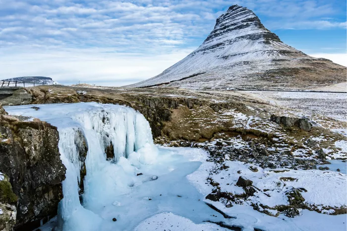 Besneeuwde puntige berg achter een bevroren waterval met blauw ijs en sneeuw