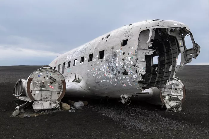 Opengereten cockpit van een vliegtuigwrak vol stickers op zwart zand
