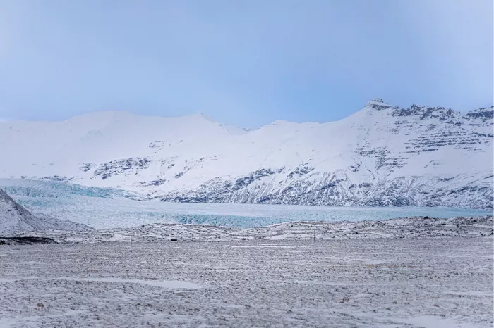 Blauwwitte gletsjertong tussen besneeuwde bergen boven een besneeuwde vlakte