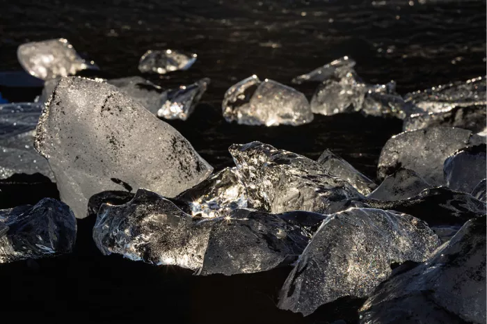 Heldere ijsblokken van dichtbij op zwart strand, oplichtend in tegenlicht