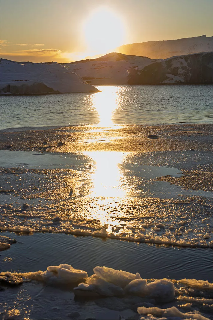 Ondergaande zon met een gouden lichtbaan over een gletsjermeer met ijsschotsen