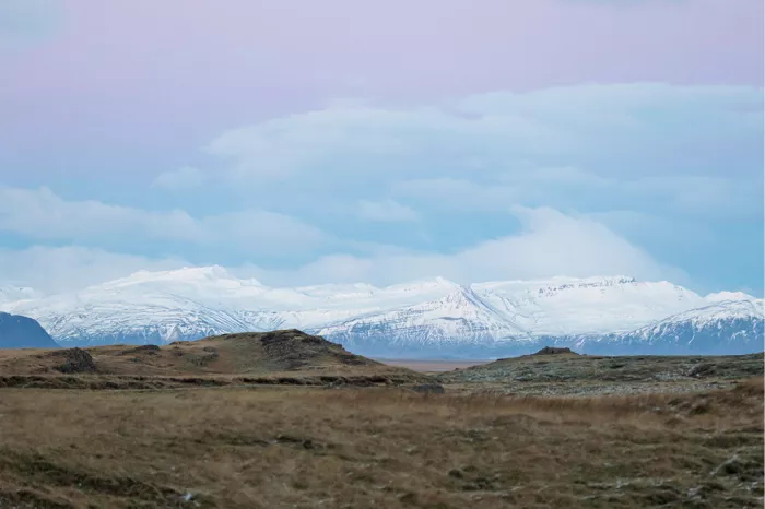 Witte besneeuwde bergen achter een vlakte met bruin gras onder een zachte wolkenlucht