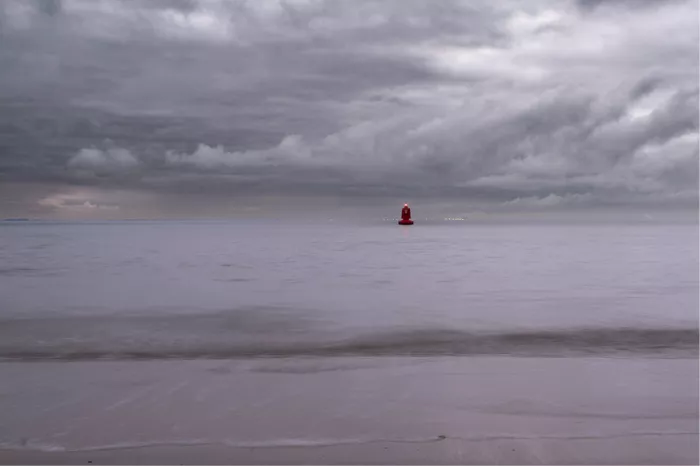Rode lichtboei op een kalme zee onder grijze wolken met een roze gloed