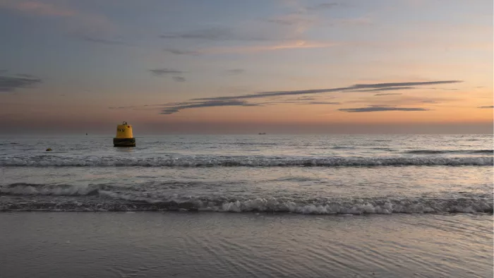 Gele boei op het water bij zonsondergang met kleine golven en een perzikkleurige lucht