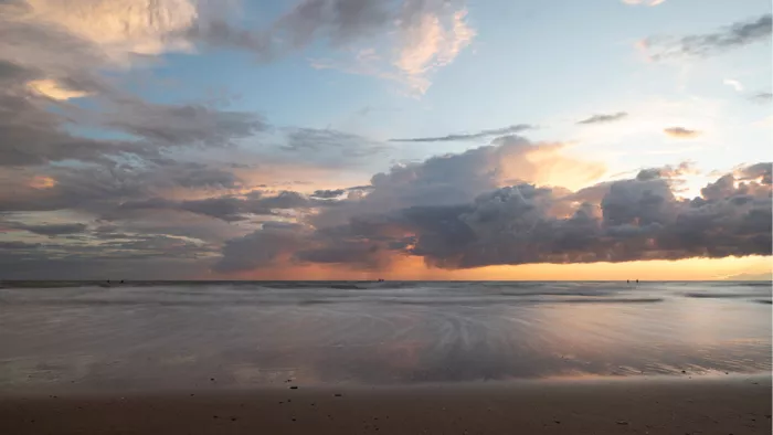 Zonsondergang aan zee met een grote wolkenbank, roze en gele kleuren en een nat glanzend strand