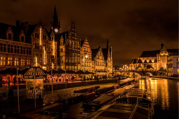 Verlichte gildehuizen langs de Graslei in Gent bij nacht met bootjes op de Leie