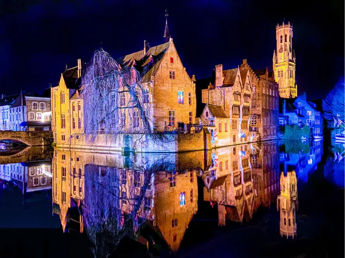 Verlichte gevels en het Belfort aan de Rozenhoedkaai in Brugge, gespiegeld in het water
