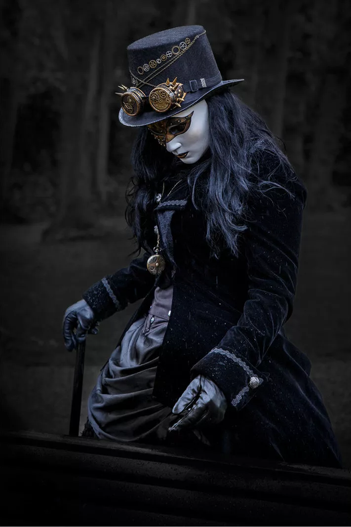 Gemaskerd meisje in steampunkkostuum met hoge hoed en wandelstok