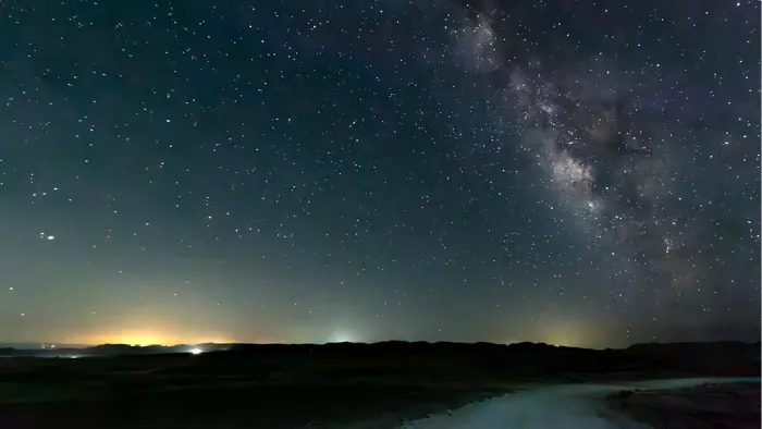 Sterrenhemel met de Melkweg boven een donkere horizon met lichtjes