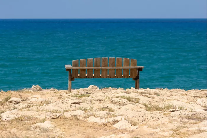 Houten bankje op een rotsige kust met uitzicht op een turquoise zee