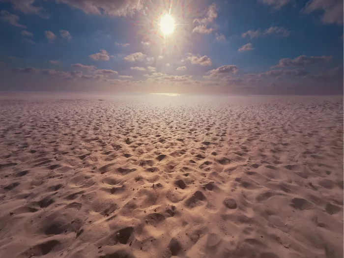 Zandvlakte met voetsporen onder een stralende zon en blauwe hemel