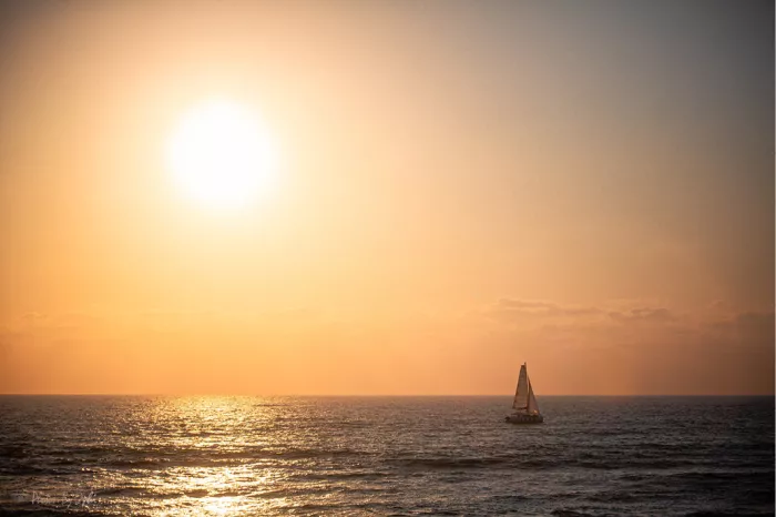 Zeilboot als silhouet op zee onder een gloeiende oranje zon