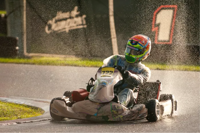 Kartcoureur met kleurrijke helm in de bocht op een nat circuit met opspattend water