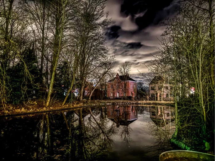 Bakstenen huis gespiegeld in een vijver tussen kale bomen bij avond