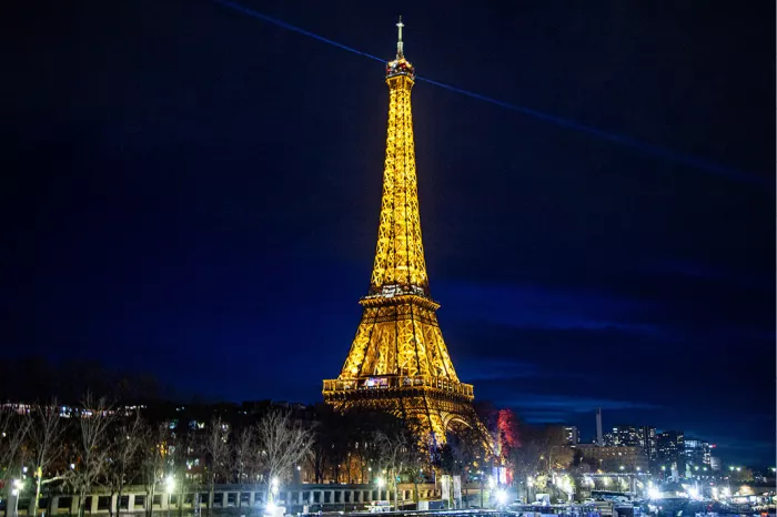 Goudgeel verlichte Eiffeltoren tegen een nachtblauwe hemel, met lichtjes langs de Seine