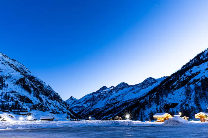 Besneeuwd bergdal in blauw licht met verlichte chalets en lantaarns onder een diepblauwe lucht