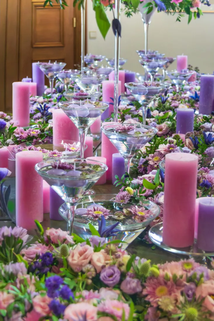 Feesttafel met roze en paarse kaarsen, martiniglazen met drijfkaarsen en bloemstukken