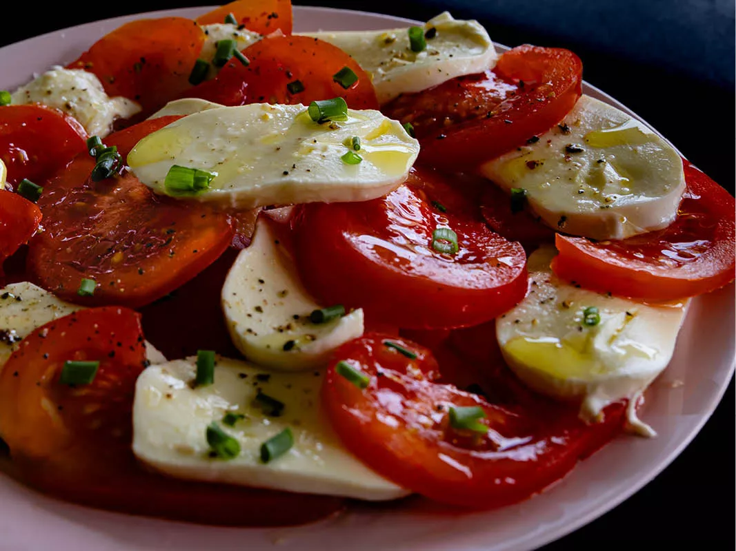 Bord salade caprese met plakken tomaat en mozzarella, olijfolie, peper en bieslook
