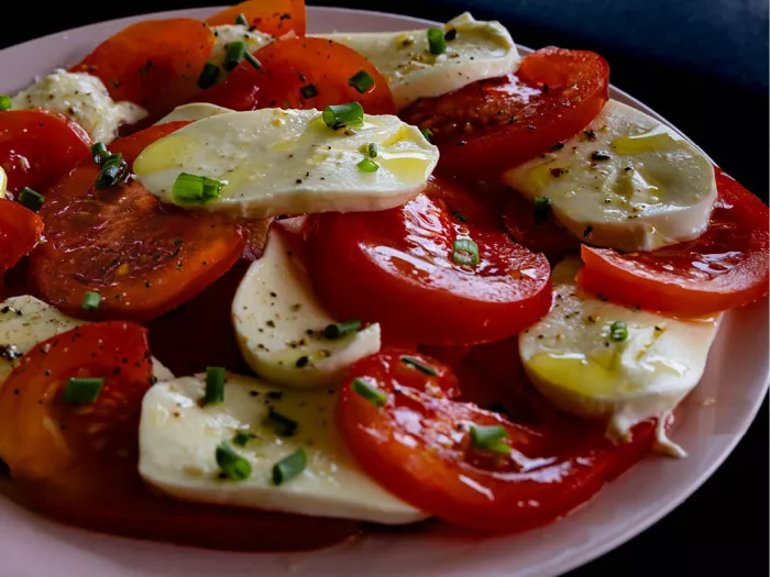 Bord salade caprese met plakken tomaat en mozzarella, olijfolie, peper en bieslook