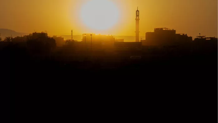 Stad met minaret in silhouet tegen een oranje lucht met een grote, laagstaande zon