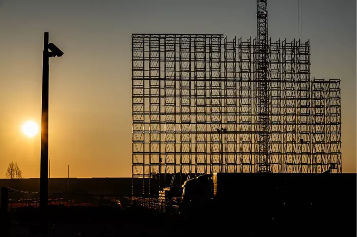 Steigerwerk en torenkraan in silhouet tegen een oranje lucht met een laagstaande zon en een lantaarnpaal