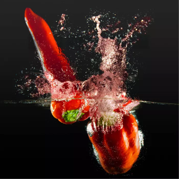 Twee rode paprika's die in water vallen met spetters en luchtbellen tegen een zwarte achtergrond