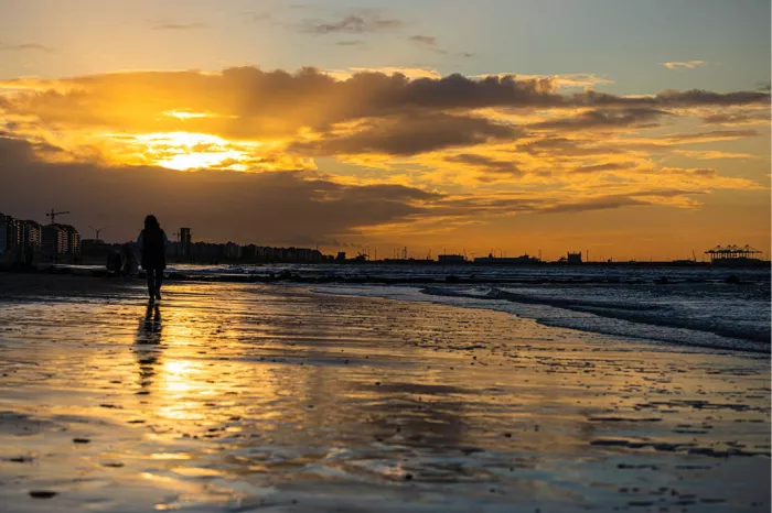 Strand bij zonsondergang met een wandelaar in silhouet en gouden reflecties op het natte zand