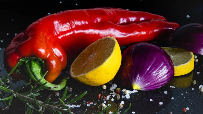 Diep verzadigde kleuren springen uit het beeld terwijl een glanzende rode puntpaprika centraal ligt tussen een doormidden gesneden citroen en een paarse ui. ceptillustraties.