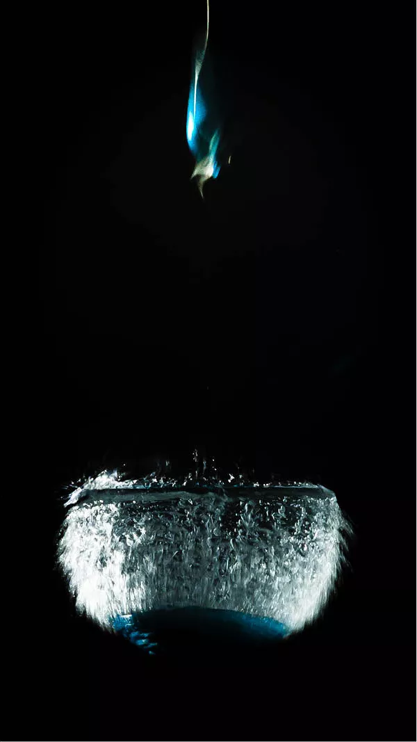 Een dichte wolk van waterdruppels barst naar buiten op het exacte moment dat een met water gevulde ballon openspat. Het bovenste gedeelte van de ballon schiet als een kleurrijke, vervormde vorm omhoog, terwijl de watermassa nog heel even haar originele contour behoudt. 